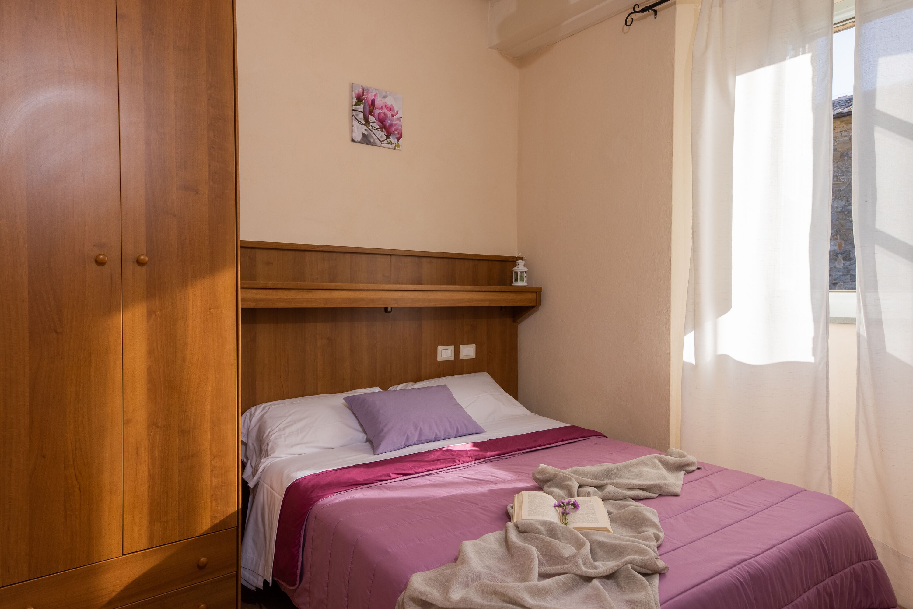 Un dormitorio con un armario de madera, una cama con colcha morada y un estante pequeño en la pared.