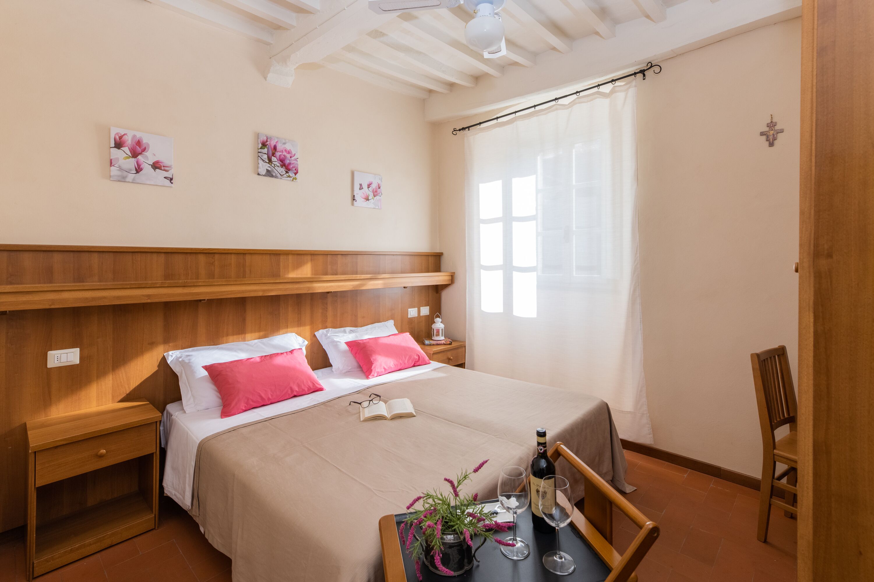 A neatly arranged bedroom with a bed, bedside tables, a small table with a bottle and glasses, and a chair.