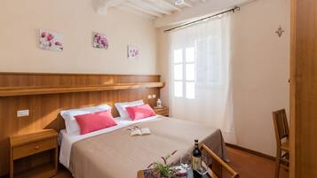 A neatly arranged bedroom with a bed, bedside tables, a small table with a bottle and glasses, and a chair.