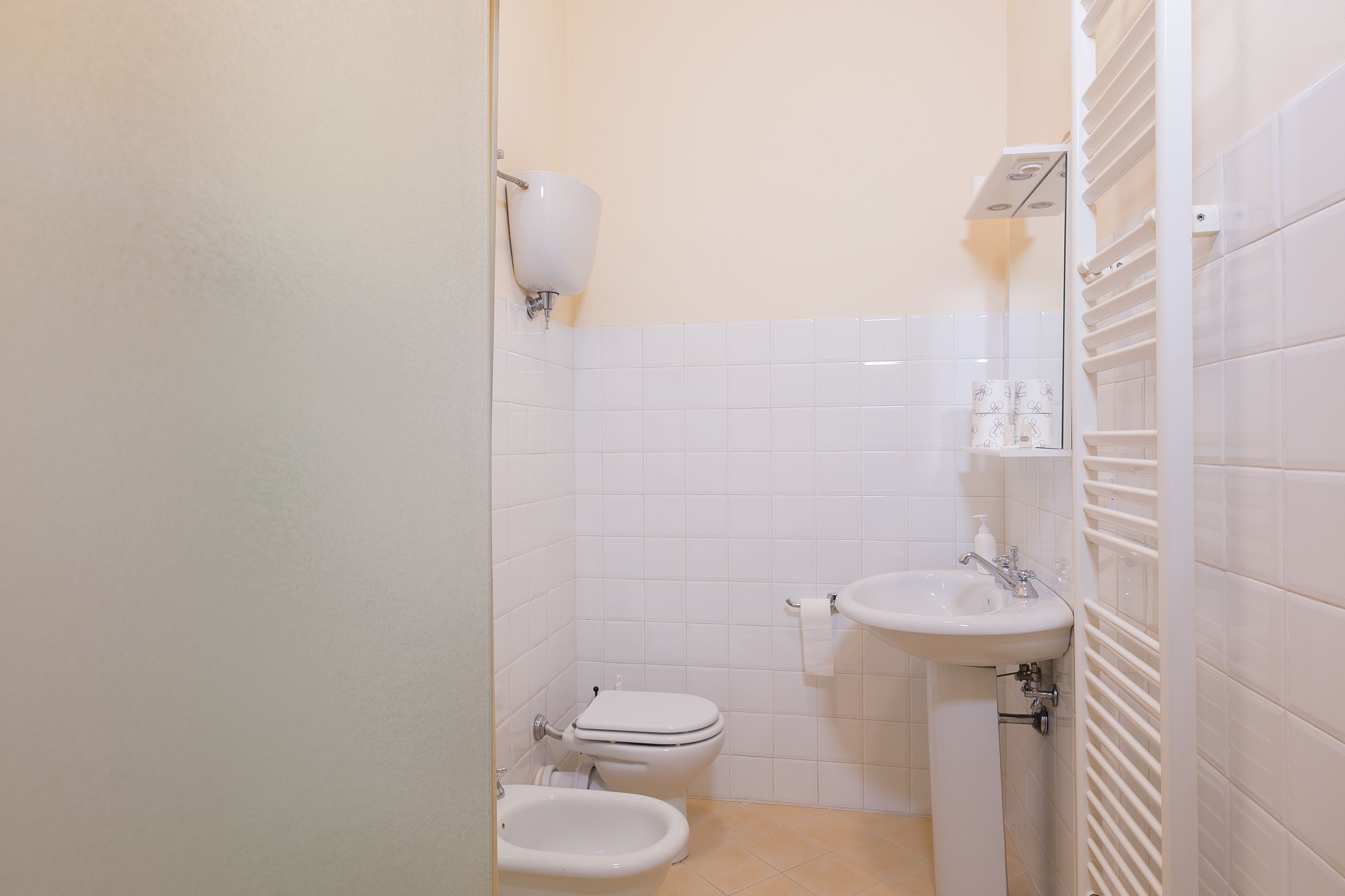 Un bagno piccolo e pulito, con piastrelle bianche, un water, un bidet e un lavandino.