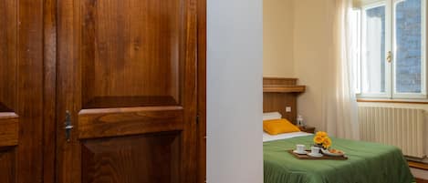 Une porte en bois, un lit recouvert d’une couverture verte, une fenêtre avec des rideaux et un radiateur.