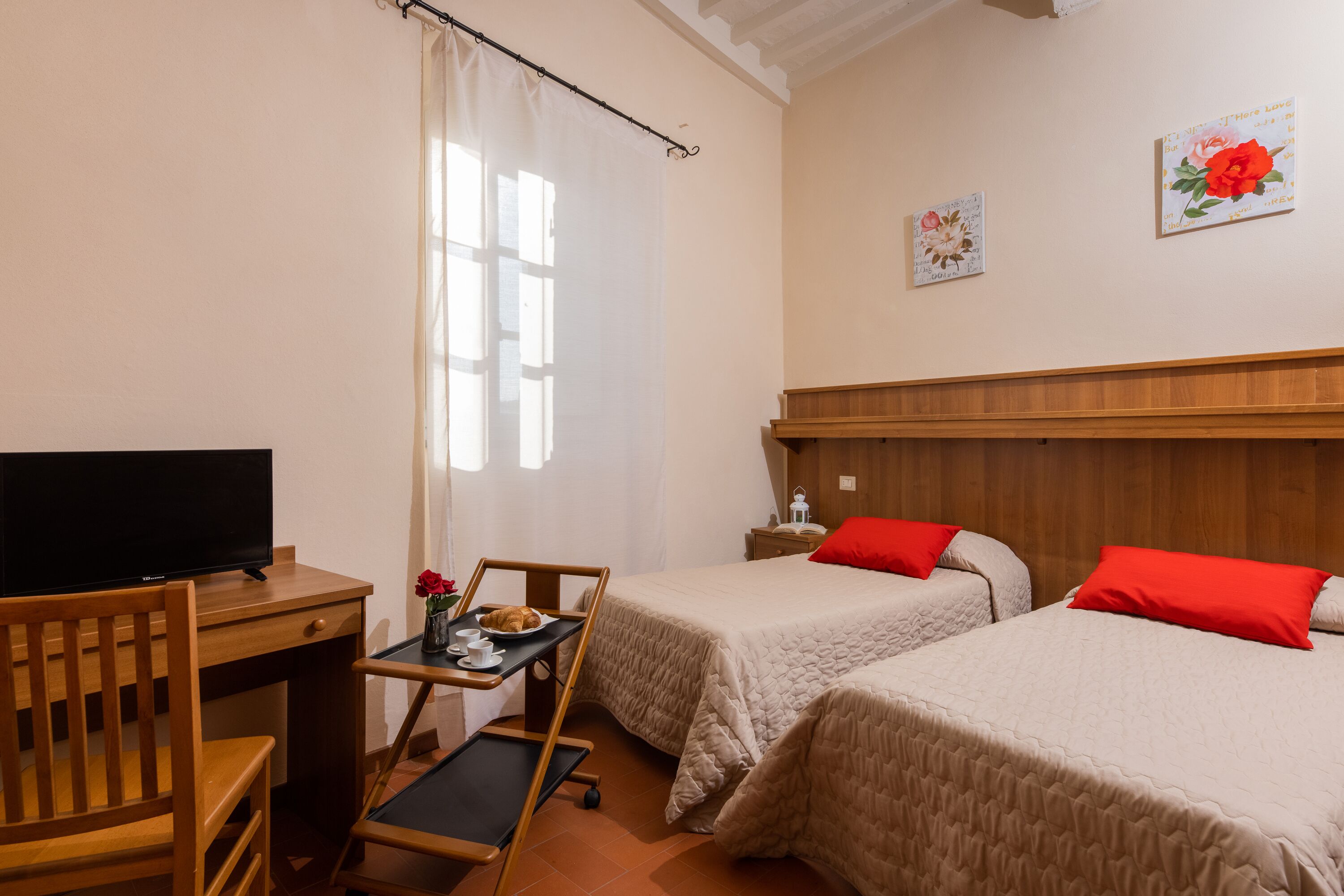 A hotel room with two beds, a desk with a TV, a small table with a tray, and a chair.