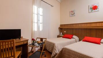 A hotel room with two beds, a desk with a TV, a small table with a tray, and a chair.