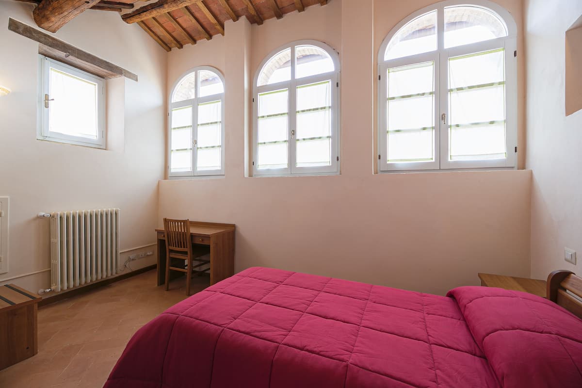A bedroom with a bed, a desk, and three arched windows.