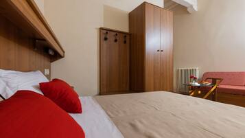 A bedroom with a bed, a wardrobe, a radiator, and a small table with a vase and flowers.