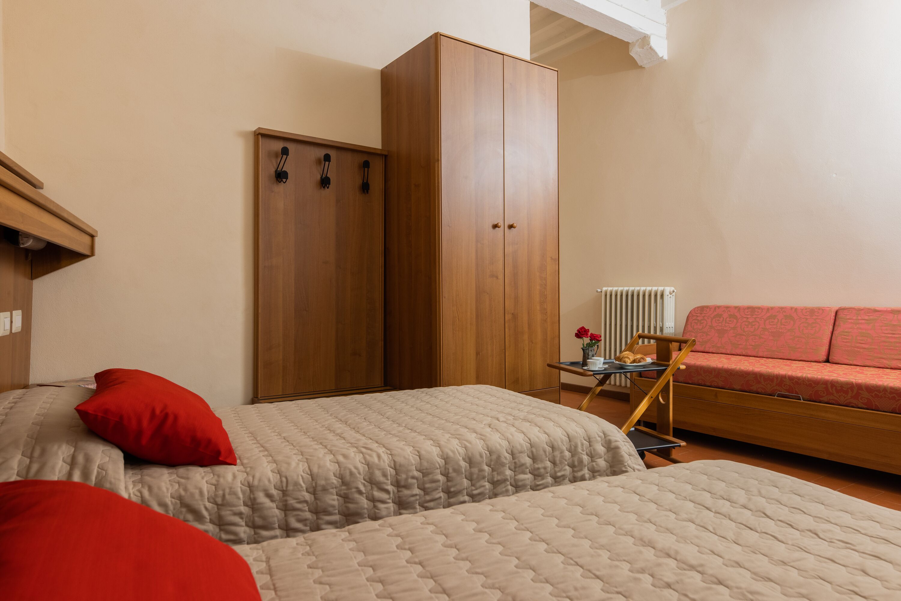 Een slaapkamer met twee bedden, een houten garderobe, een rode bank en een klein tafeltje met een bloevas.