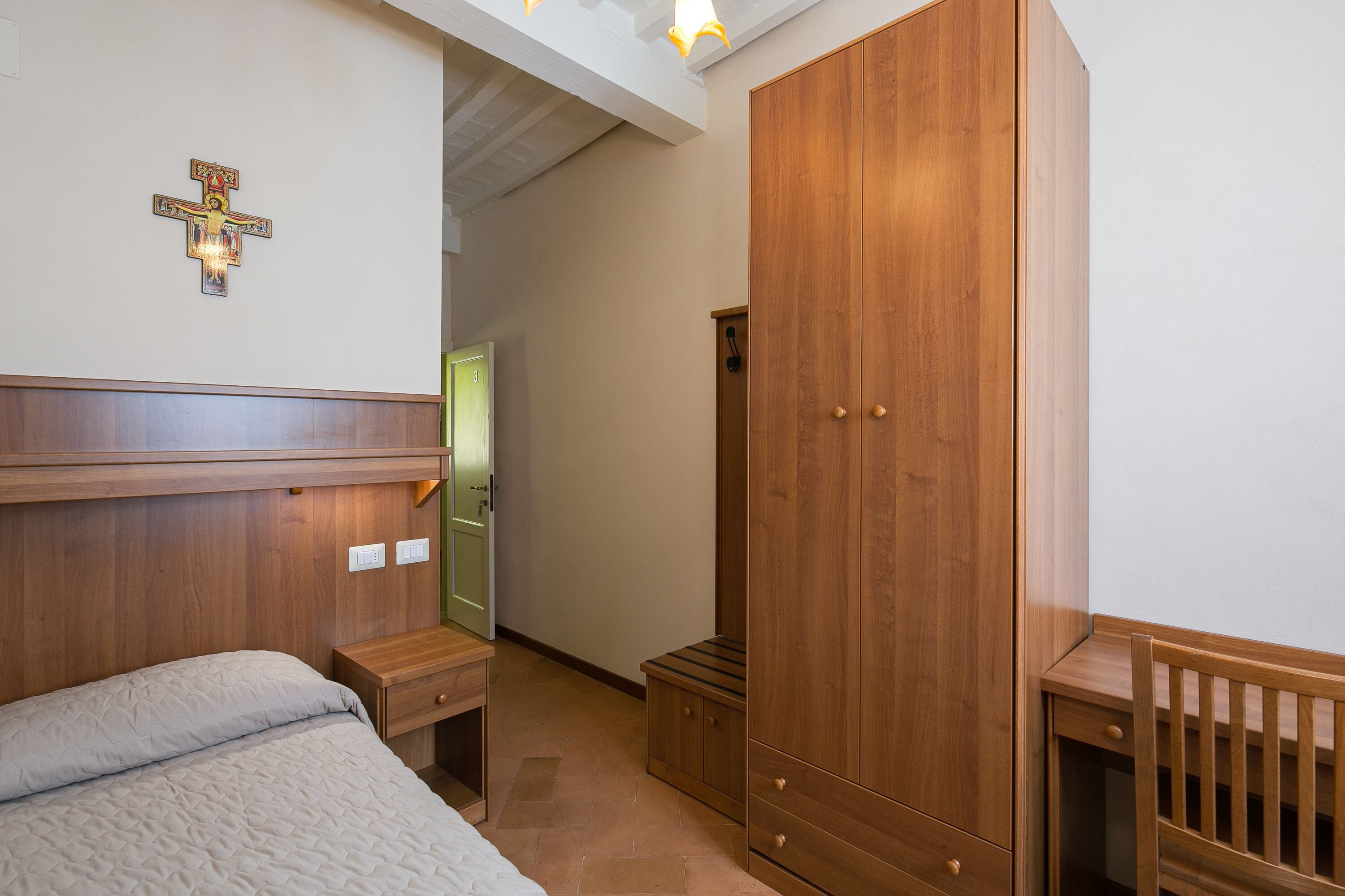 A bedroom with a wooden headboard, a wooden wardrobe, a bedside table, and a crib.