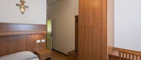A bedroom with a wooden headboard, a wooden wardrobe, a bedside table, and a crib.