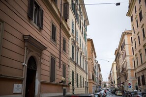A narrow street lined with historic buildings, featuring classic architecture and a mix of residential and commercial spaces. - Chroma Italy - Chroma Deka (Rome)