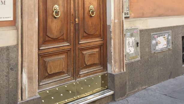 A large wooden double door with ornate metal handles, set within an arched entrance with decorative moldings. - Chroma Italy - Chroma Deka (Rome)