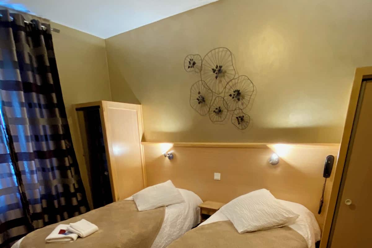Habitación de hotel con dos camas, cabecera de madera, decoración en la pared, un teléfono y una puerta.