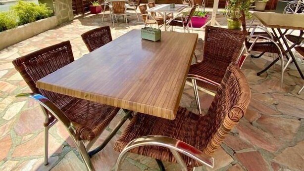 Un patio al aire libre con suelo de piedra, muebles de mimbre y sombrillas rojas.