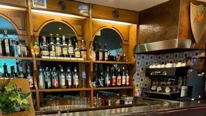 Un área de bar con estantes de madera llenos de botellas, una máquina de café y dos taburetes de bar de madera con cojines azules.