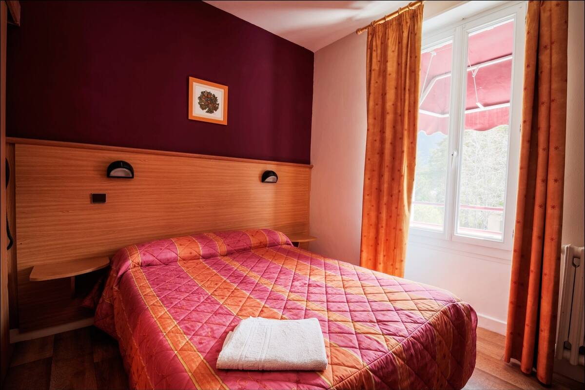 Un dormitorio con cabecera de madera, colcha acolchada en tonos rosa y naranja, y una toalla blanca sobre la cama.