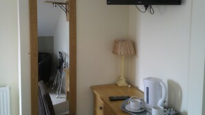 A hotel room with a wooden desk, a chair, a television mounted on the wall, a lamp, and a tray with cups and a kettle. - The Crown Hotel (Corwen)