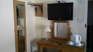 A hotel room with a wooden desk, a television mounted above it, a mirror, a lamp, a remote control, and a tray with a coffee maker and cups. - The Crown Hotel (Corwen)