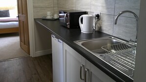 A compact kitchen with a microwave, kettle, and sink. - The Crown Hotel (Corwen)