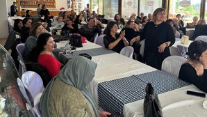 A restaurant with multiple tables, some with white tablecloths and others with patterned ones. There are people seated and standing, and a counter with a display case in the background. - Selim Sultan Otel (Menderes)
