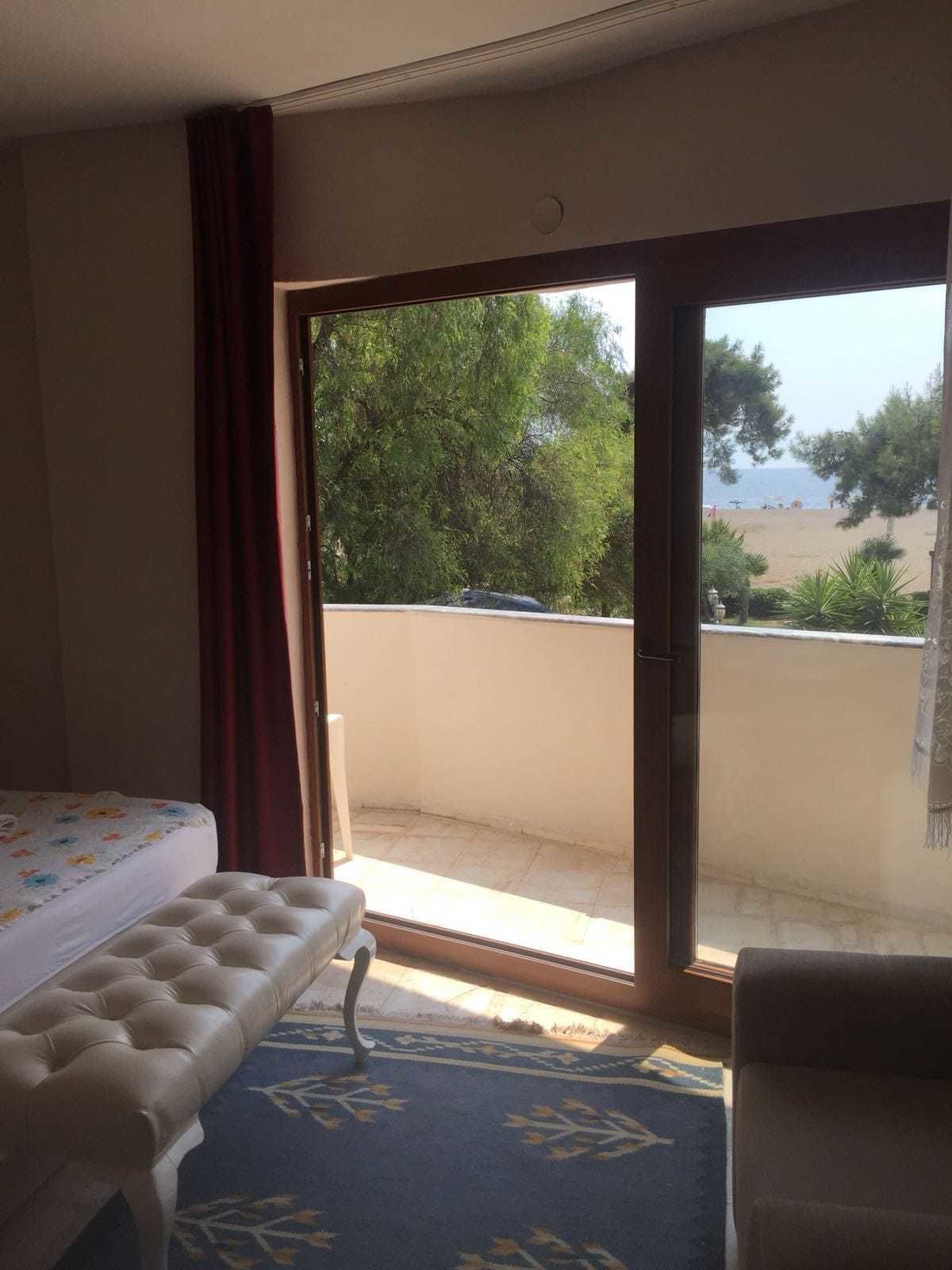 Habitación de hotel con cama, un banco, vista a una playa y un balcón con puerta.