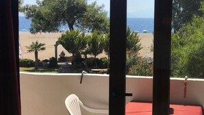 A balcony with a view of a beach, a table with a red tablecloth, and a white chair. - Selim Sultan Otel (Menderes)