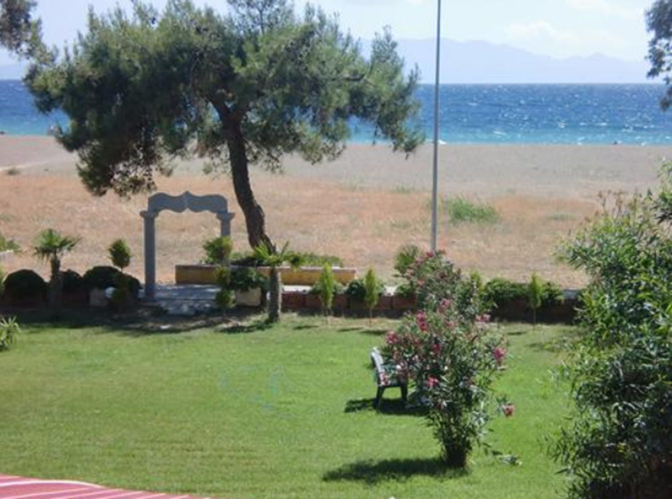 A grassy area with a stone archway, a bench, and a view of the sea.