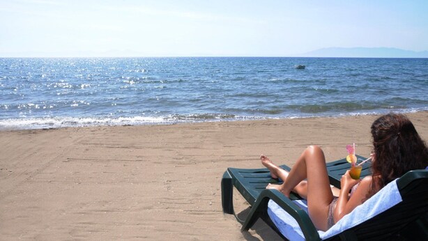 A person relaxing on a beach chair with a drink, facing the ocean. - Selim Sultan Otel (Menderes)