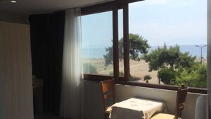 A hotel room with a bed, a small table, and a chair. There is a window with a view of the beach and the sea. - Selim Sultan Otel (Menderes)