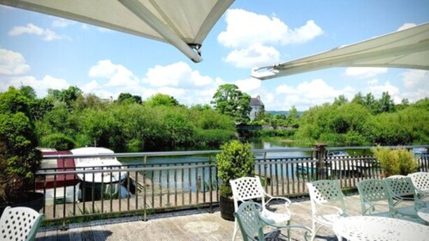 A terrace with outdoor seating, a view of a river, and a distant building. - Lord Bagenal Inn (Leighlinbridge)
