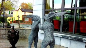 A sculpture of two figures in a courtyard with a stone floor, a large window, and a building in the background. - Lord Bagenal Inn (Leighlinbridge)