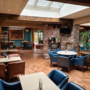 A restaurant with a high ceiling, brick walls, and a skylight. There are tables and chairs for dining, and a television mounted on the wall. - Lord Bagenal Inn (Leighlinbridge)