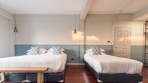 A room with two beds, a wooden table, and a door. - Karnvela Phuket (Phuket)
