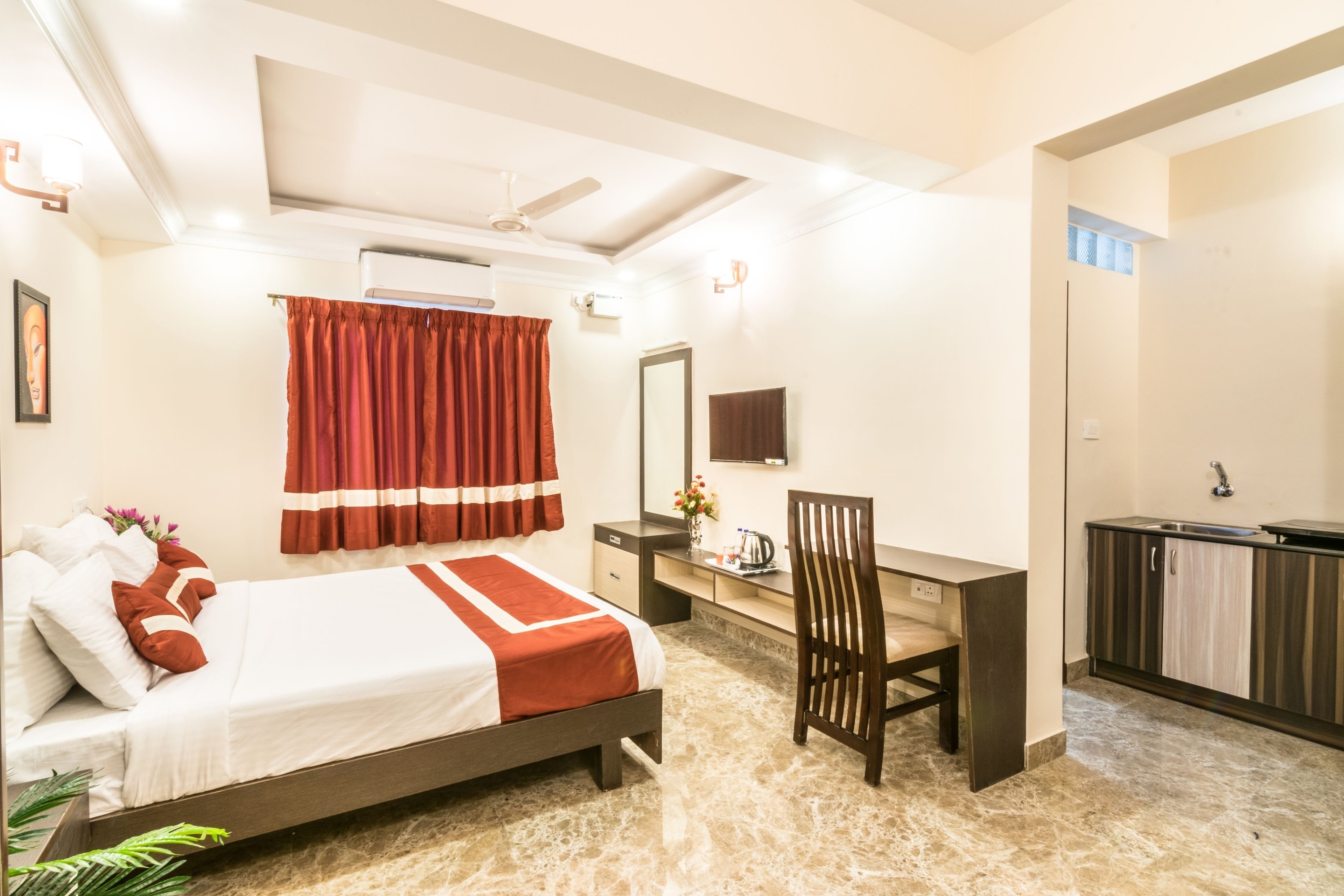 A hotel room with a bed, desk, chair, and a small kitchenette.