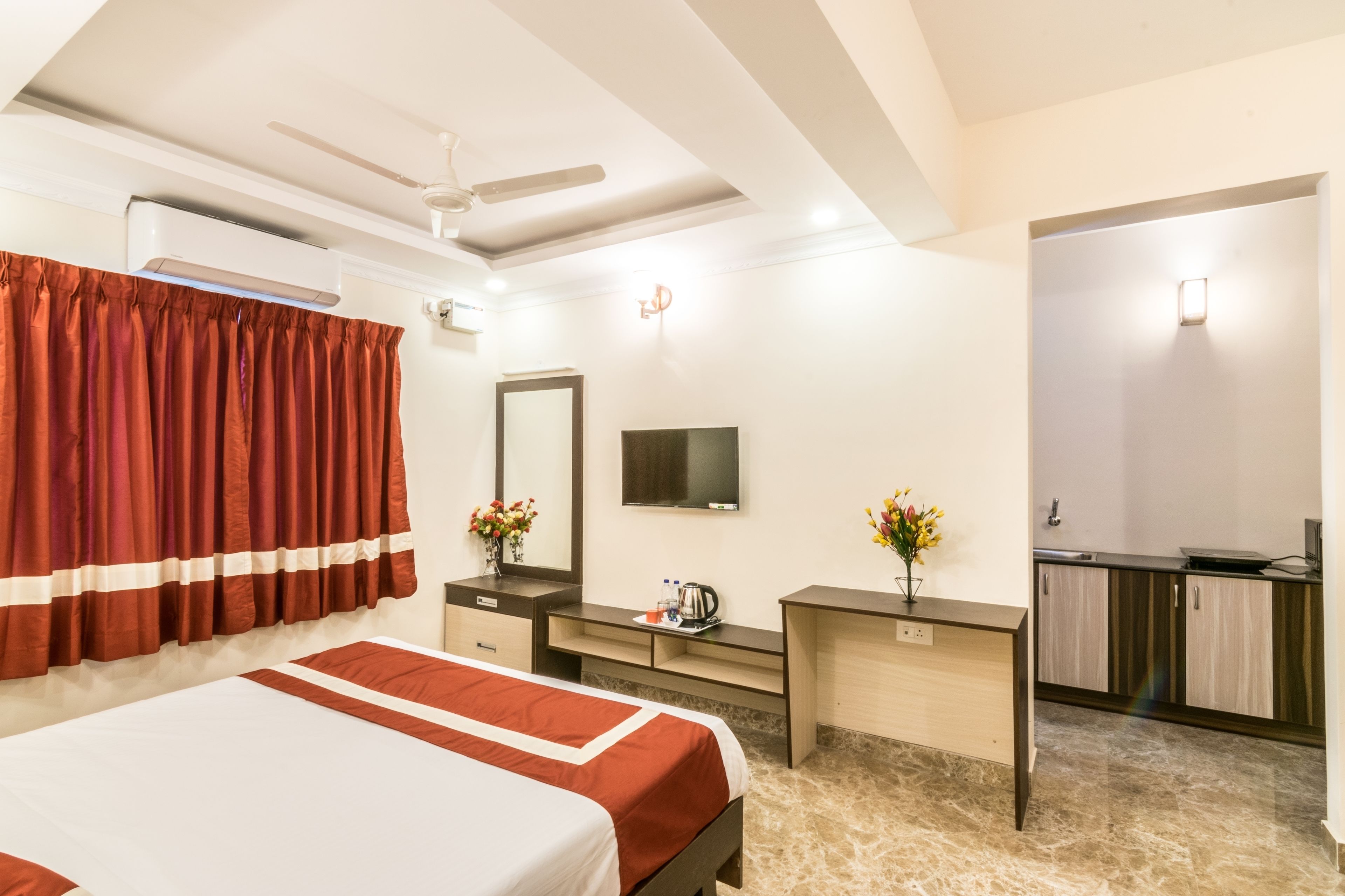 A hotel room with a bed, a desk, a mirror, a TV, and a kitchenette.