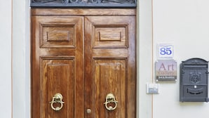 Puerta doble de madera con un arco metálico decorativo encima, un letrero que indica una galería de arte y un buzón.