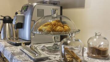 Una mesa con un mantel de encaje, con croissants en un expositor de vidrio, una cafetera y un hervidor de agua.