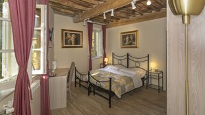 Un dormitorio con piso de madera, una cama con colcha estampada, una mesita de noche con lámpara y una ventana con cortinas.