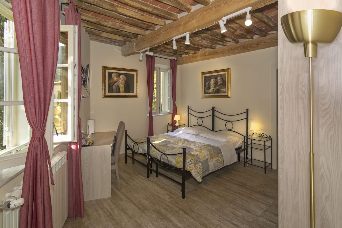 Ein Schlafzimmer mit Holzboden, einem Bett mit gemustertem Überwurf, einem Nachttisch mit Lampe und einem Fenster mit Vorhängen.