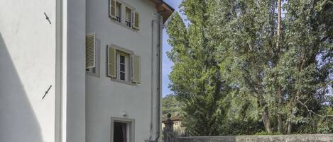 A two-story building with a white facade, shutters, and a stone wall.