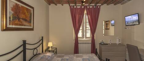 Un dormitorio con cama, cómoda, televisor y ventana con cortinas.