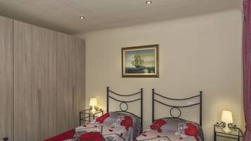 A bedroom with two beds, a wooden wardrobe, a painting of a ship on the wall, and two bedside tables with lamps.