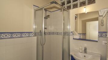 A bathroom with a glass shower enclosure, a sink with a mirror, and decorative blue tiles.