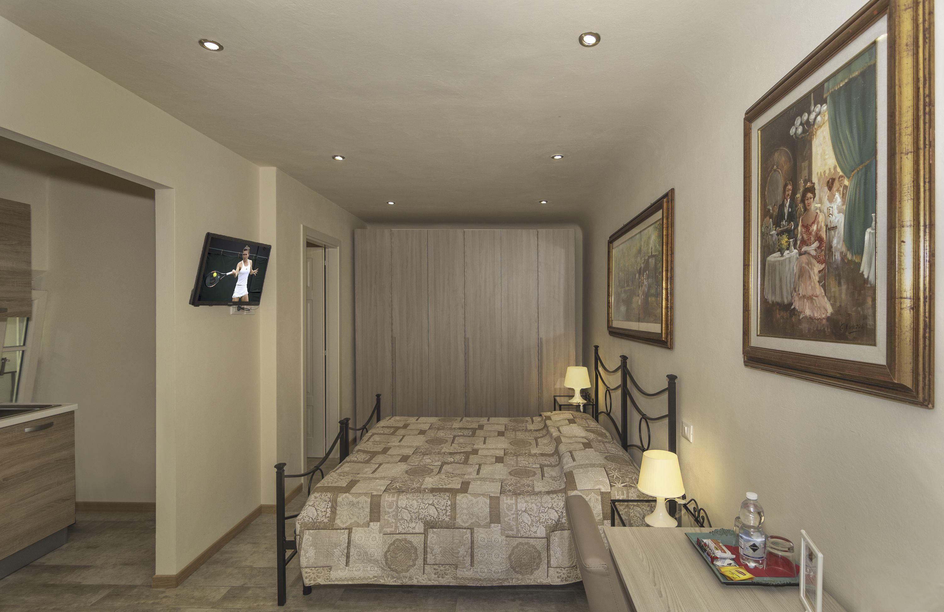A hotel room with a bed, bedside table, lamp, and a TV mounted on the wall.
