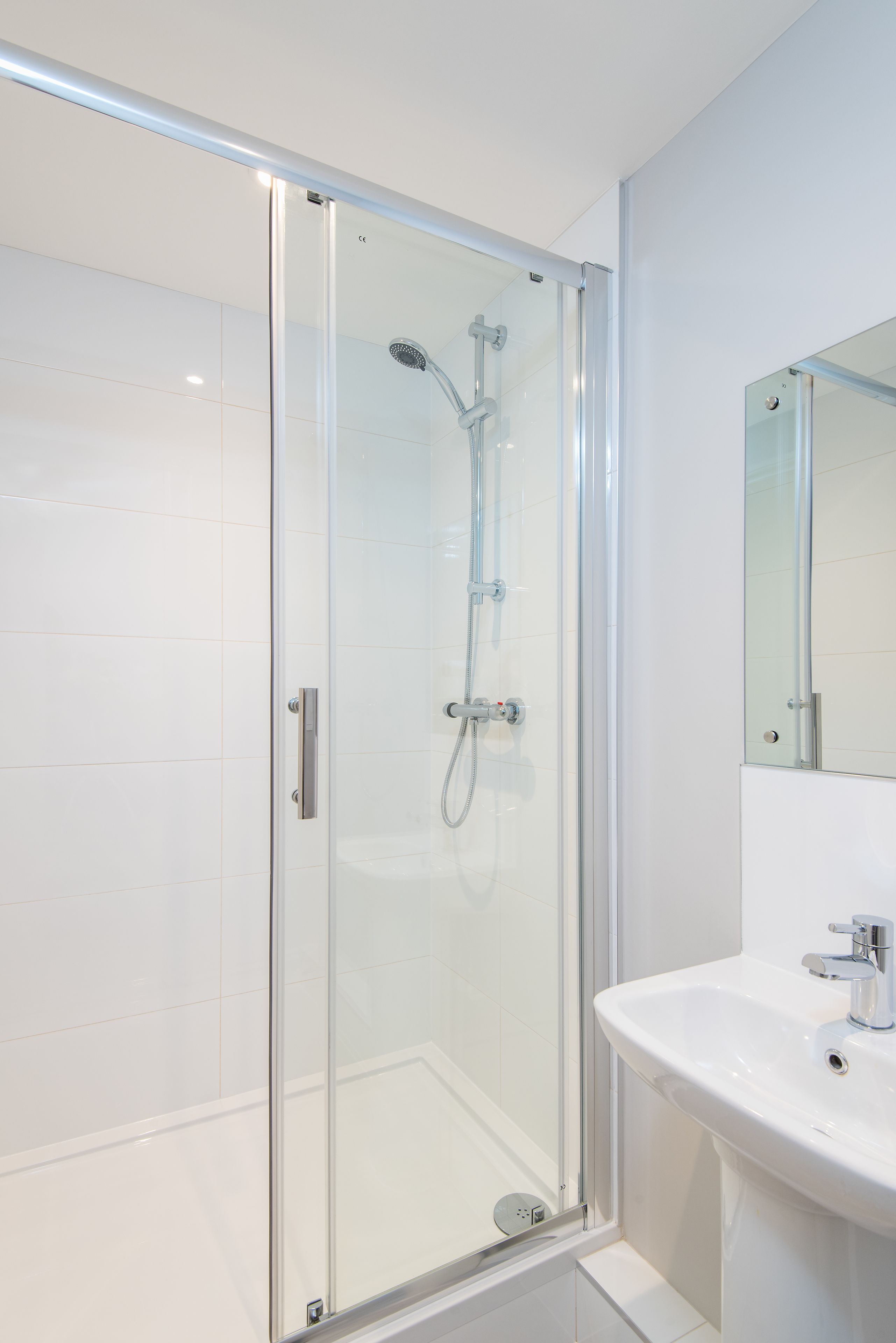 A modern bathroom with a glass-enclosed shower, a white sink, and a mirror.