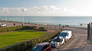 Una carretera costera con una valla verde, coches estacionados y una vista despejada del mar.