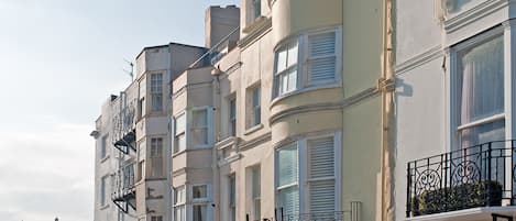 A row of multi-story buildings with balconies, a brick sidewalk, and a street lamp.