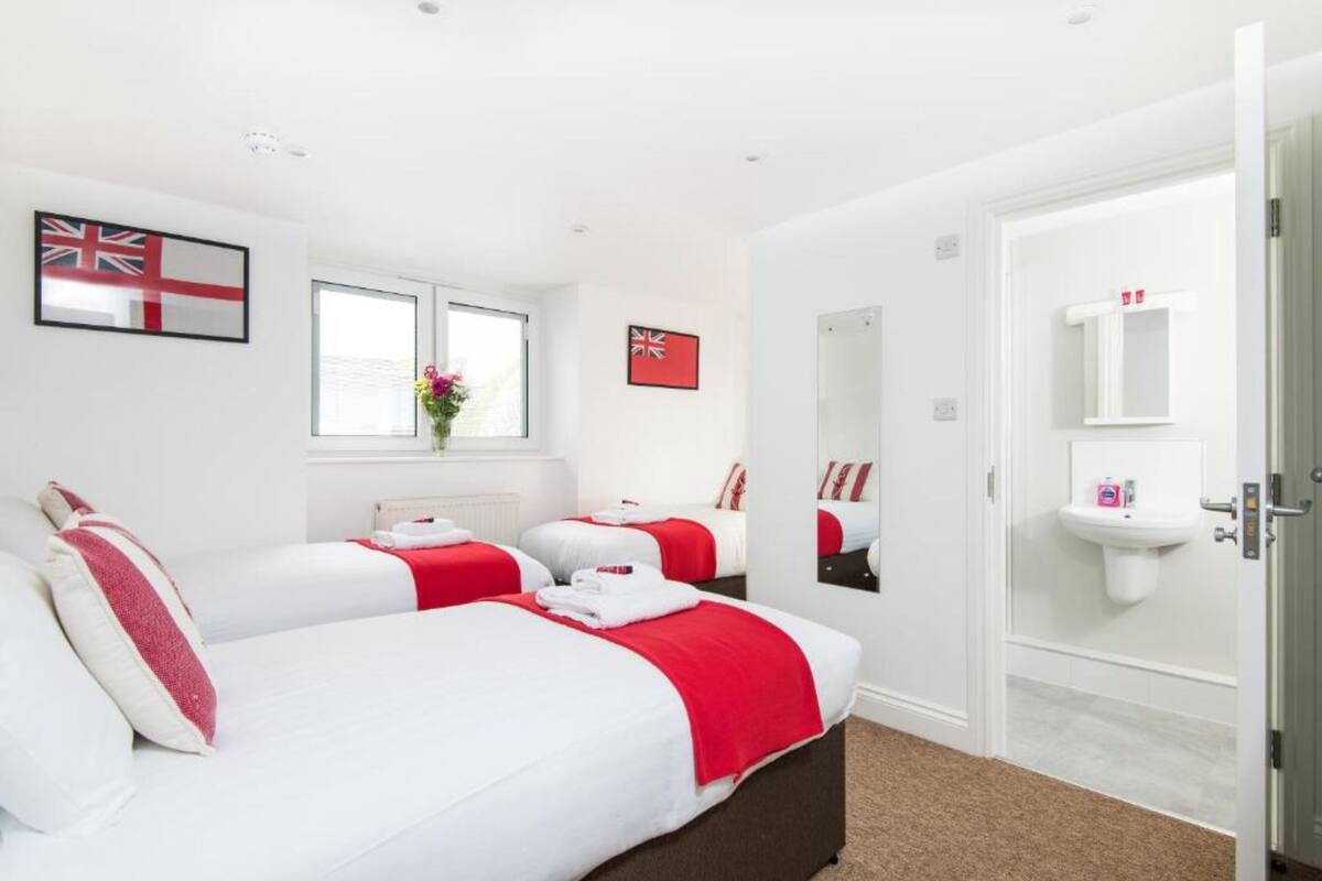 A hotel room with three beds, a window with a view, a sink, and a mirror.