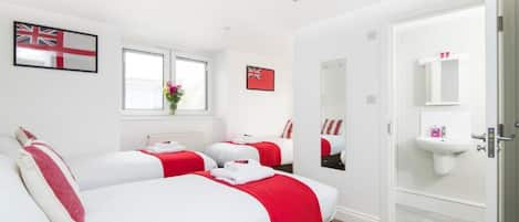 A hotel room with three beds, a window with a view, a sink, and a mirror.