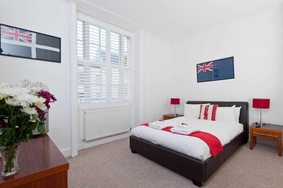 A neatly arranged bedroom with a bed, bedside tables, and a window with blinds.