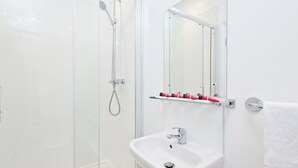 Un baño moderno con cabina de ducha de vidrio, un lavabo blanco y una repisa de vidrio con artículos de aseo.