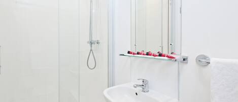 A modern bathroom with a glass shower enclosure, a white sink, and a glass shelf with toiletries.